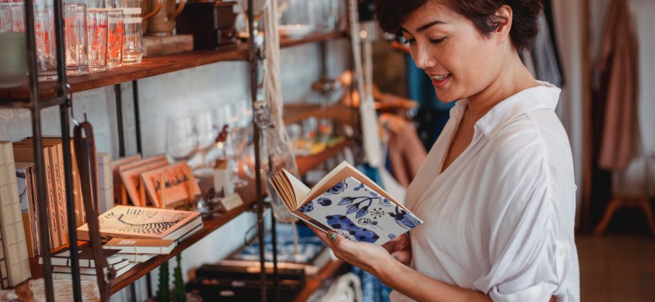 gorgeous asian young lady reading novel in vintage boutique