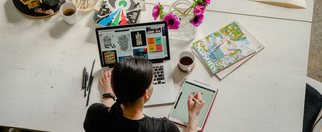 photo of woman writing on tablet computer while using laptop