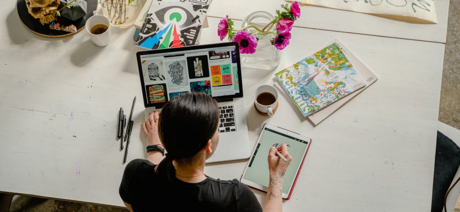 photo of woman writing on tablet computer while using laptop